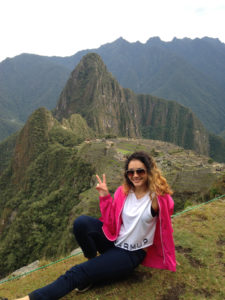 Leslie Peralta sits on a rock with Guatemalan mountains in the background andd shows the peace sign.