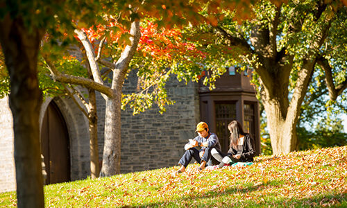 Students sitting on campus in the fall.